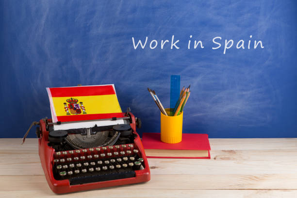 istock work abroad concept - red typewriter, flag of Spain, books on table and blackboard with text 
