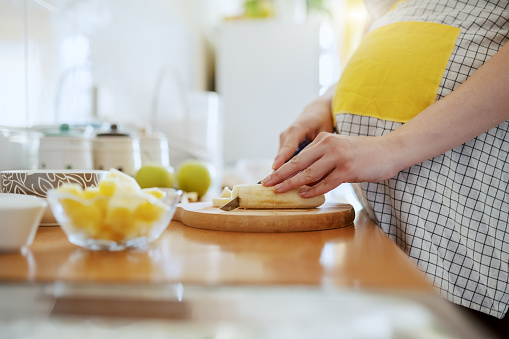Close up of Caucasian pregnant woman in apron cutting banana and preparing healthy breakfast.