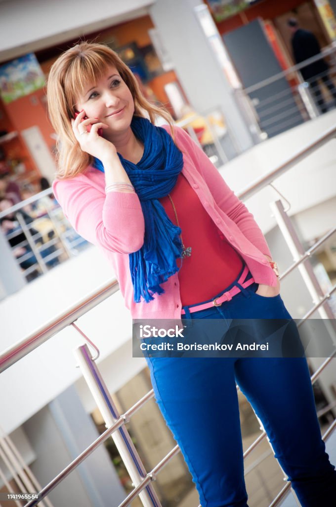 The girl in the store talking on the phone. Red European in bright summer clothes. Adult Stock Photo