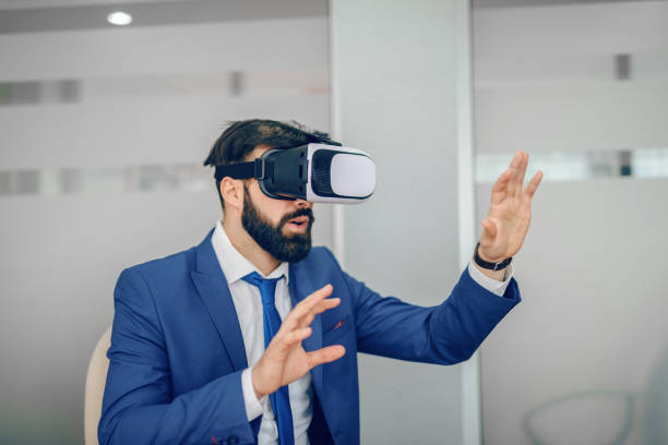 istock Young Caucasian bearded businessman in blue suit using vr goggles at office. 1141965583