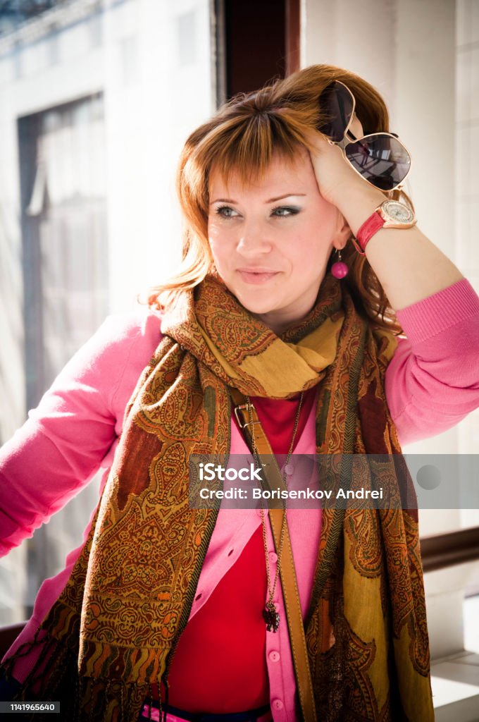 A girl in bright modern clothes stands in front of a large window in a store. White Koha, copper hair color. Adult Stock Photo