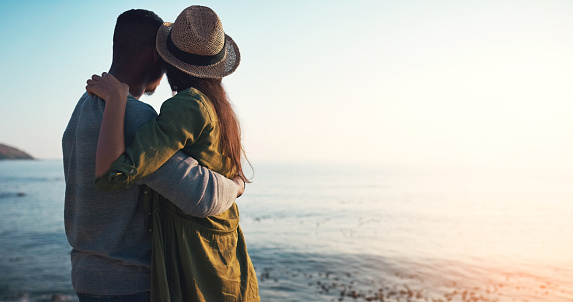 Rearview shot of an affectionate young couple embracing each other on the beach at sunset