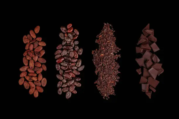 Photo of Peeled, chopped cocoa beans and  pile chopped, milled chocolate isolated on black background