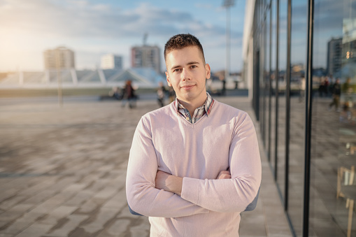 Smiling cute Caucasian man dressed elegant standing on rooftop with crossed arms.