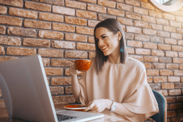 istock Smiling Caucasian brunette dressed elegant drinking coffee in cafeteria and looking at laptop. 1141970024