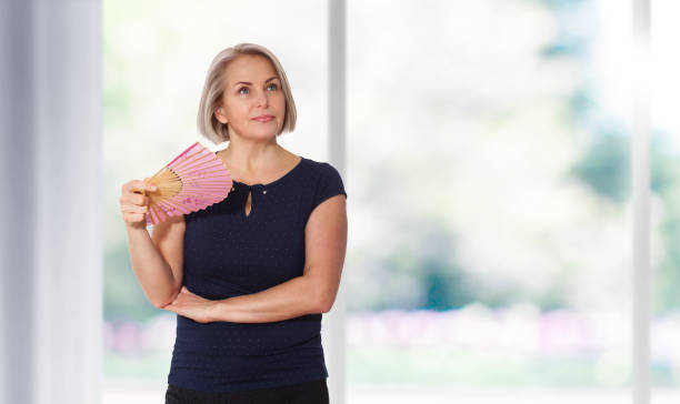 attraente donna di mezza età rilassante con ventilatore. donna matura che sperimenta il lavaggio a caldo dalla menopausa - menopause foto e immagini stock