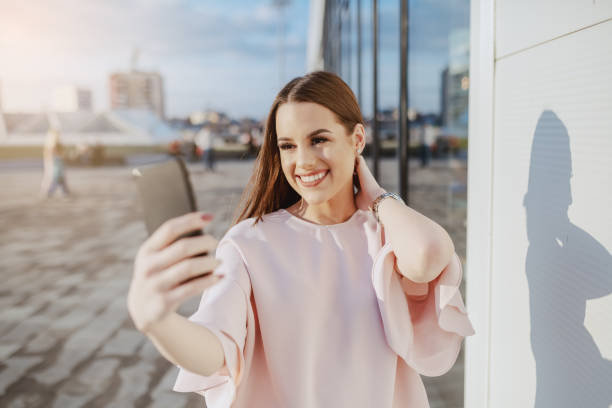 istock Gorgeous smiling Caucasian brunette dressed elegant standing outdoors and taking selfie. 1141971429