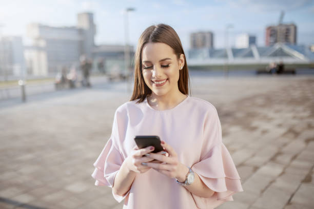 istock Charming Caucasian brunette dressed elegant smiling and using smart phone on rooftop. 1141971892
