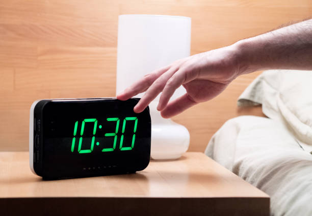 Man reaching to turning off digital alarm clock in the morning at 10.30 a.m. young man in bed reaching to turn alarm clock off at 10.30 a.m. alarm clock snooze stock pictures, royalty-free photos & images