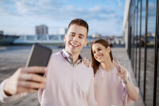 Cute cheerful Caucasian couple standing outdoors and taking selfie.