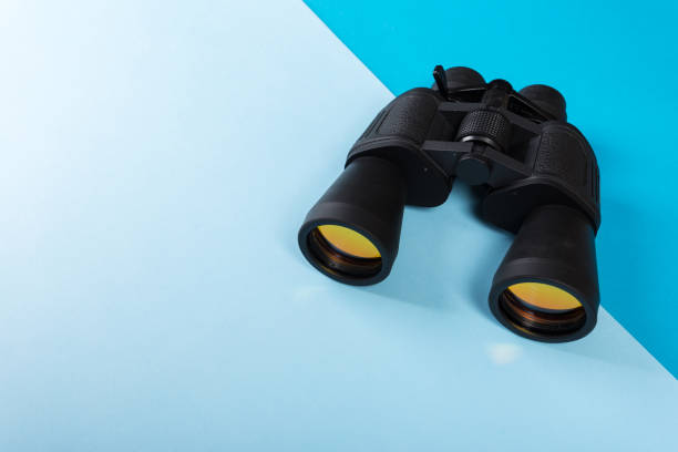 istock Black binoculars with orange lens on blue background 1141976030