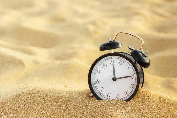 istock Vacation time. Alarm clock on the sand 1141978411