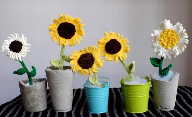 Amazing five flower vase on table make from craftsmanship by knit art from yarn, white and yellow sunflower with green leaves in jar so nice for decoration home, beautiful woolen flora in front view