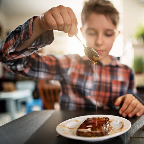 mały chłopiec wylewający miód na bochenek chleba pełnoziarnistego - breakfast bread table drop zdjęcia i obrazy z banku zdjęć