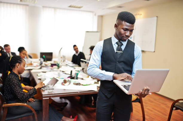 Face of handsome african business man, holding laptop on the background of business peoples multiracial team meeting, sitting in office table.