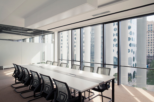 View of bright contemporary business conference meeting room with urban city in windows executive corporate in a row downtown skyscraper