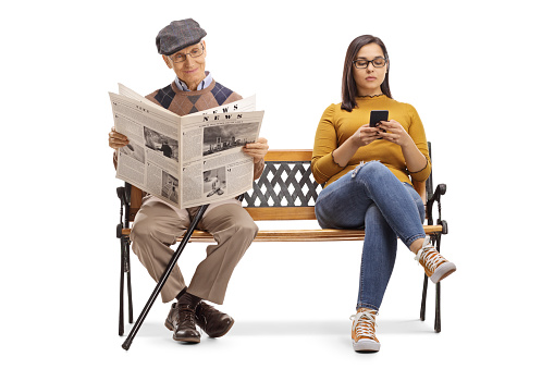Full length portrait of a young female with a mobile phone and a senior man reading a newspaper on a bench isolated on white background