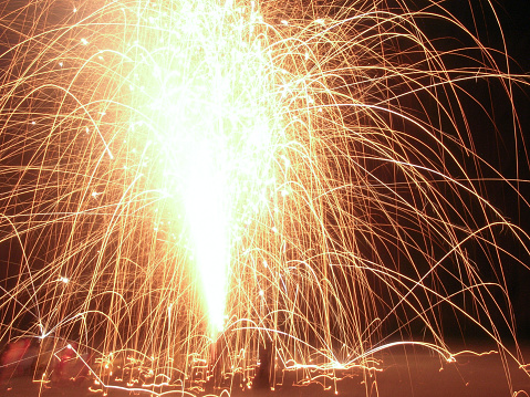 A golden colored fountain firework exploding high in the air like fire, with sparks flying every.