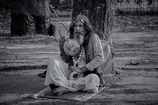 A baul singing folk music with ektara (a type of string instrument) under tree shade in Amra Kunja (mango garden) of Shantiniketan.\nShantiniketan (means abode of peace), a small town near Bolpur, at Birbum district of West Bengal. Famous for Visva-Bharati University, which was founded by Nobel laureate Rabindranath Tagore. Rabindranath Tagore’s vision of setting up a school along the lines of the previously existing system of gurukul (a residential school where students lived with their teacher/guru, a tradition present in India from Vedic period) – was the foundation stone of Visva-Bharati.\nToday it has become one of India's most renowned places of higher learning.\nPhoto taken inside Visva-Bharati University campus, on 12/17/2016.