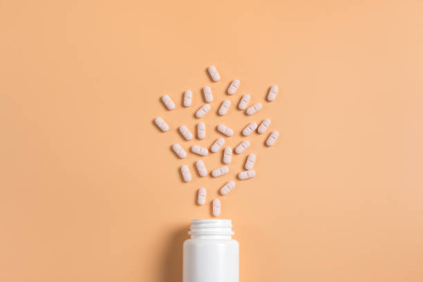 istock Pink pills, tablets and white bottle on orange background. Copy space for text 1142003974