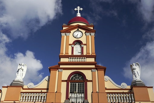 Spanish Church Facade Building Exterior with Cross Shape, Tower Clock and Statues of Angels Colonial Architecture Detail near San Jose Costa Rica City Center