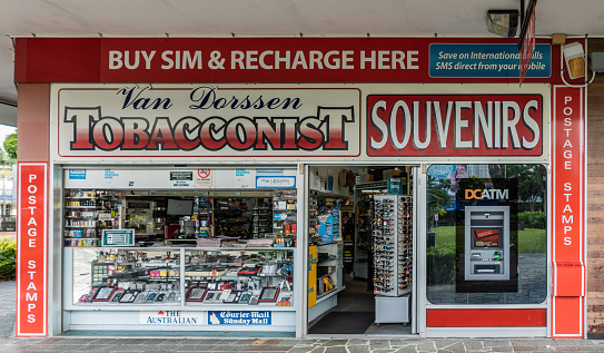 Cairns, Australia - February 17, 2019: Tobacconist Van Dorssen on corner of Shield and Abbot Streets has windows framed in red. Selling souvenirs and newspapers, too. ATM machine in window.