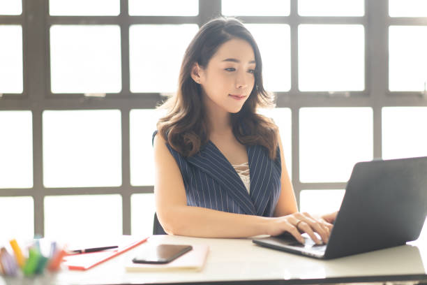 Portrait of smiling pretty young Asian business woman working on laptop in her workstation. Portrait of smiling pretty young Asian business woman working on laptop in her workstation chinese woman stock pictures, royalty-free photos & images