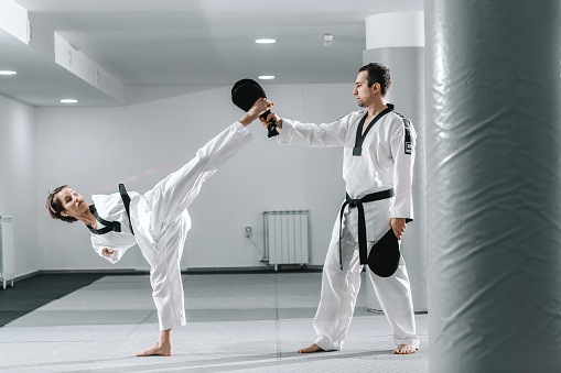 Caucasian handicapped highly motivated girl practicing taekwondo with her training. Girl kicking kick target.