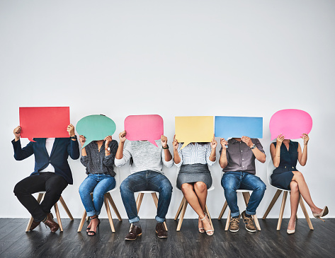 Studio shot of a group of young businesspeople holding colorful speech bubbles in line against a grey background