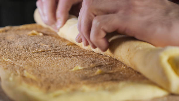 el chef baker enrolla la masa con canela, azúcar y mantequilla en un rollo sobre la mesa. - food industry manufacturing human hand fotografías e imágenes de stock