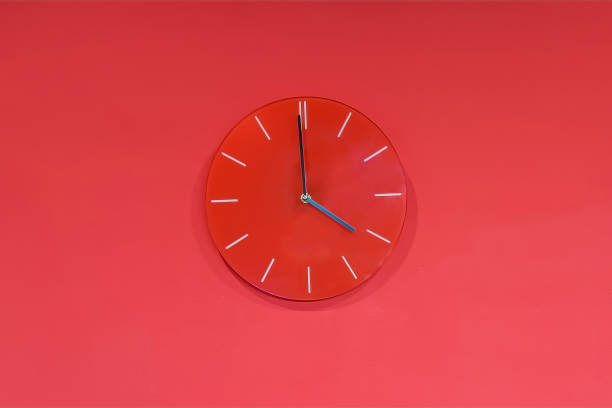 Red round modern analog glass clocks hang on a red wall. Shows the current time 4:00 pm stock photo