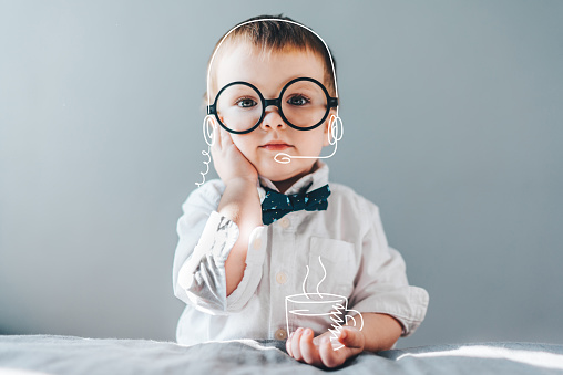Cute little genius. Baby boy wearing smart outfit and eye glasses working as call center operator answering several people and drinking imaginery coffee. Children and technologies concept.