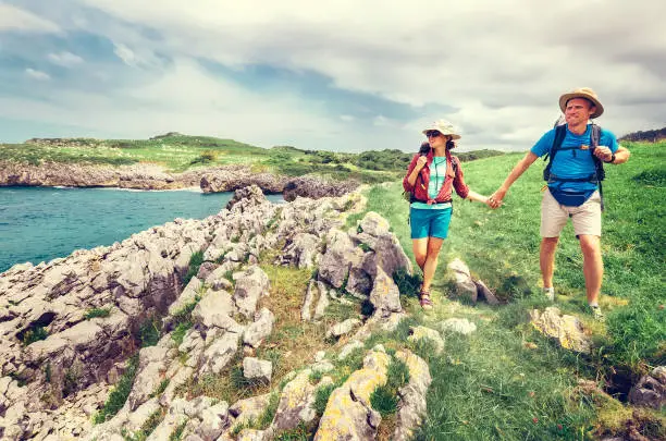 Photo of Couple backpacker travelers walk on ocean rocky coast. Asturias. Spain