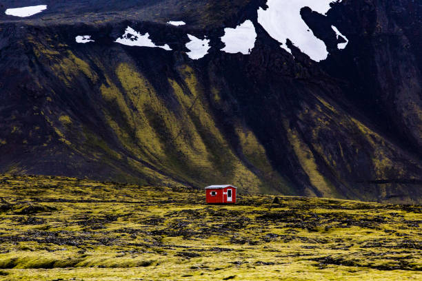 Isolated orange shelter near moss-covered mountains with snow patches in Reykjanesfólkvangur nature park Iceland on a cloudy dark summer day stock photo