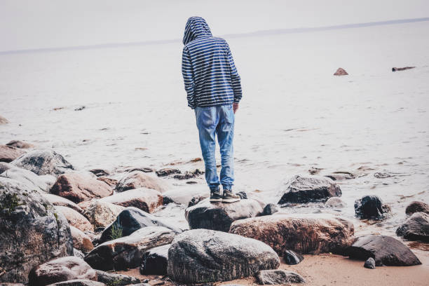 A young man stands on the shore and enjoys the sea landscape