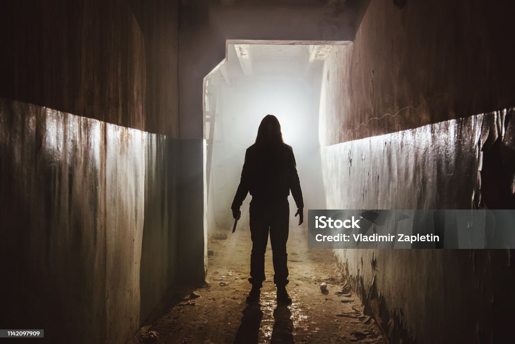 Creepy silhouette with knife  in the dark abandoned building. Horror about maniac concept Creepy silhouette with knife  in the dark abandoned building. Horror about maniac concept. Serial Killings Stock Photo