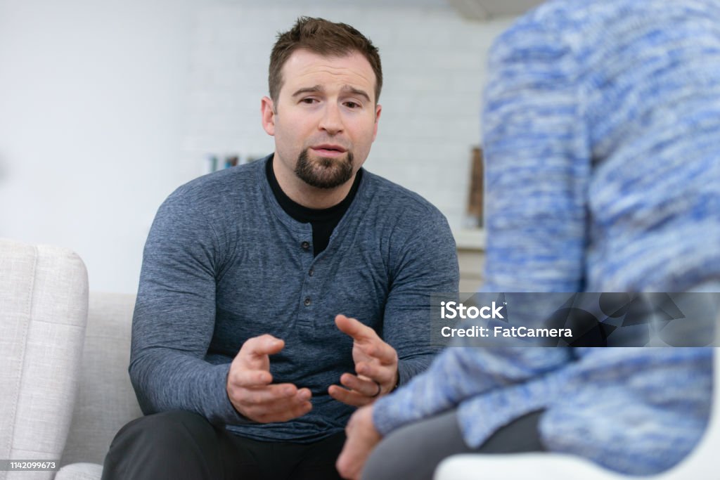 Upset man in therapy A young husband sits across from his therapist looking defeated. He is upset because he realizes that he has not been as attentive to his wife's needs as he should be. Discussion Stock Photo