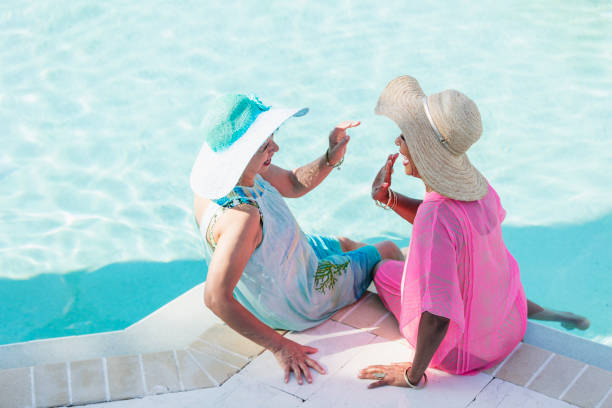 istock Two senior women sitting on pool deck, high-five 1142107686