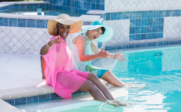 istock Two senior women sitting on pool deck, feet in water 1142108248