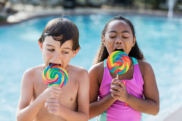 istock Two multi-ethnic children sitting by pool with lollipops 1142109194
