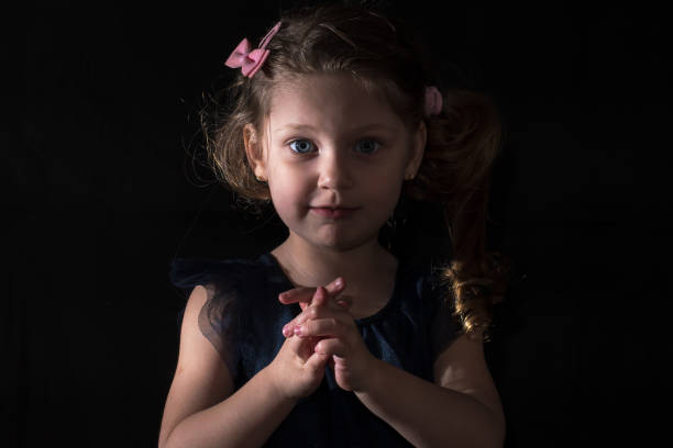 Portrait of little cover girl with freckles in doll image isolated in shadow, looking at camera. Smiling kid 6-7 year old in white dress at black background. Fashion style concept. Copy ad text space