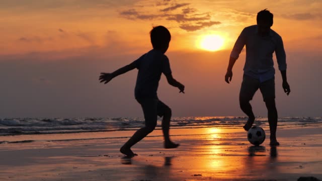 Silhouette happy father and son having fun playing football on the beach at sunset.Happy family enjoy summer vacation on the beach.Holiday travel concept.Vacations - iStock