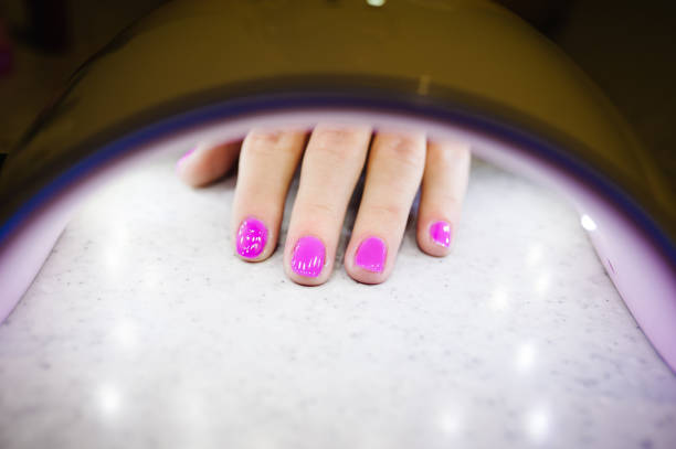 istock Woman hand inside lamp for nails on table close up. UV lamp for drying nails with gel method. violet nails dried in the lamp 1142135916