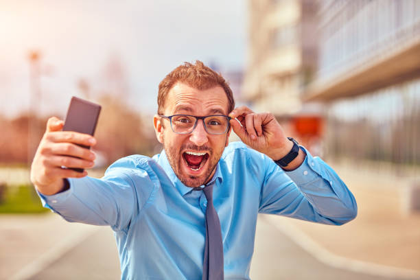 istock Funny businessman with thumbs up while using smartphone outdoors. 1142136575