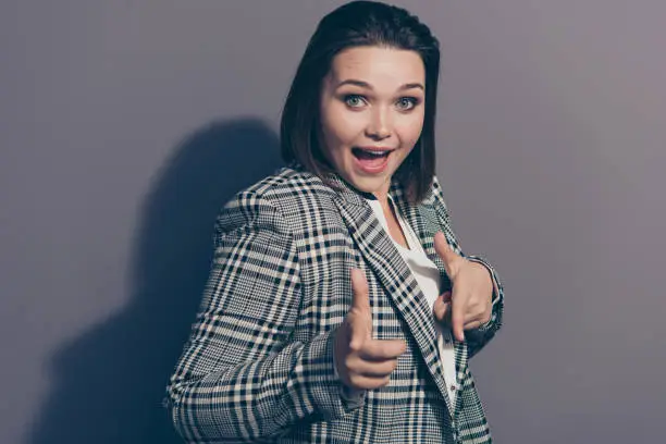 Closeup photo portrait of cheerful beautiful pretty ecstatic secretary banker lawyer pointing on camera with forefinger wearing plaid blazer isolated grey background.