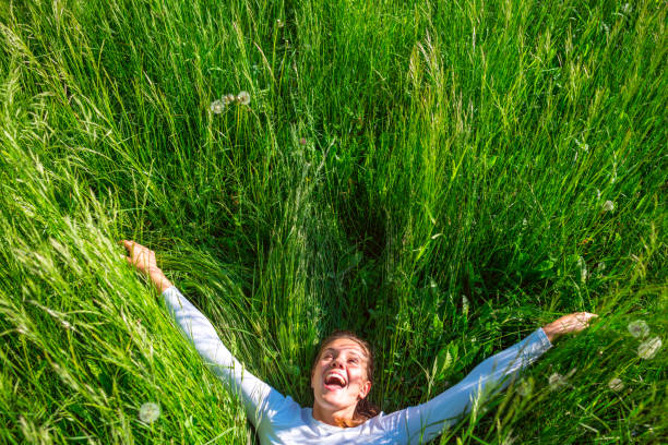Cheerful Young Woman With Arms Outstretched Lying in Grass.