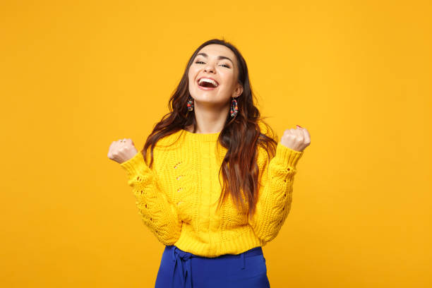 istock Laughing cheerful young woman in sweater, blue trousers looking camera, doing winner gesture isolated on yellow orange wall background. People sincere emotions, lifestyle concept. Mock up copy space. 1142149193