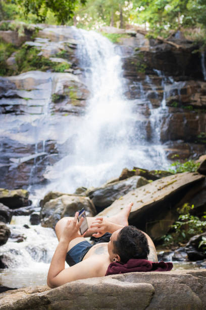 istock Man using cell phone on the rock at waterfall 1142153261