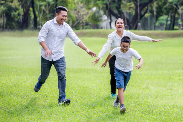 happy asian Family, parents and their children running around  in park together. father mother and son having fun and laughing outdoors . cheerful stock photo
