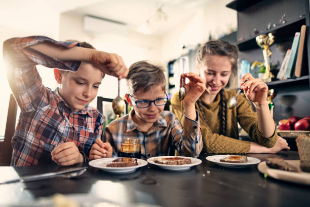 dzieci wylewające miód na bochenki chleba pełnoziarnistego - breakfast bread table drop zdjęcia i obrazy z banku zdjęć